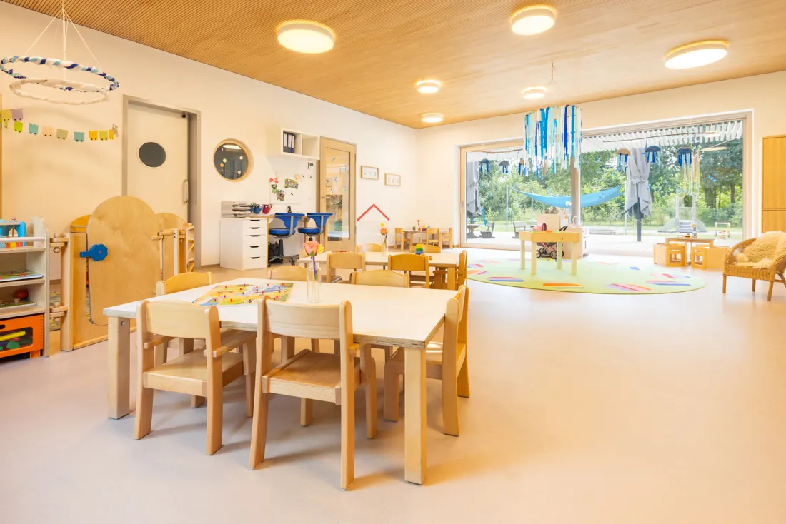 Ein Gruppenraum in einer Kindertagesst&auml;tte mit einem Tisch und mehreren St&uuml;hlen, bereit f&uuml;r Aktivit&auml;ten und Spiele.