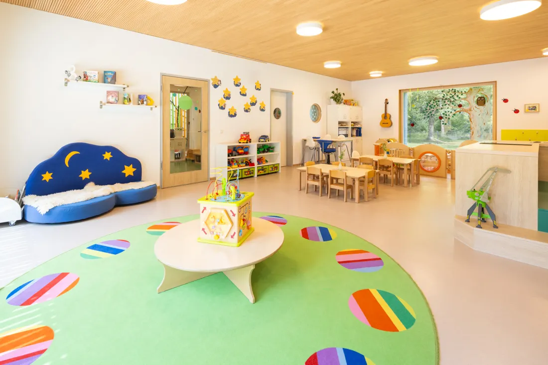 Bunter Gruppenraum des Kindergartens mit buntem Teppich, vielen Spielzeugen und Tischen und St&uuml;hlen, ideal zum Spielen und Lernen